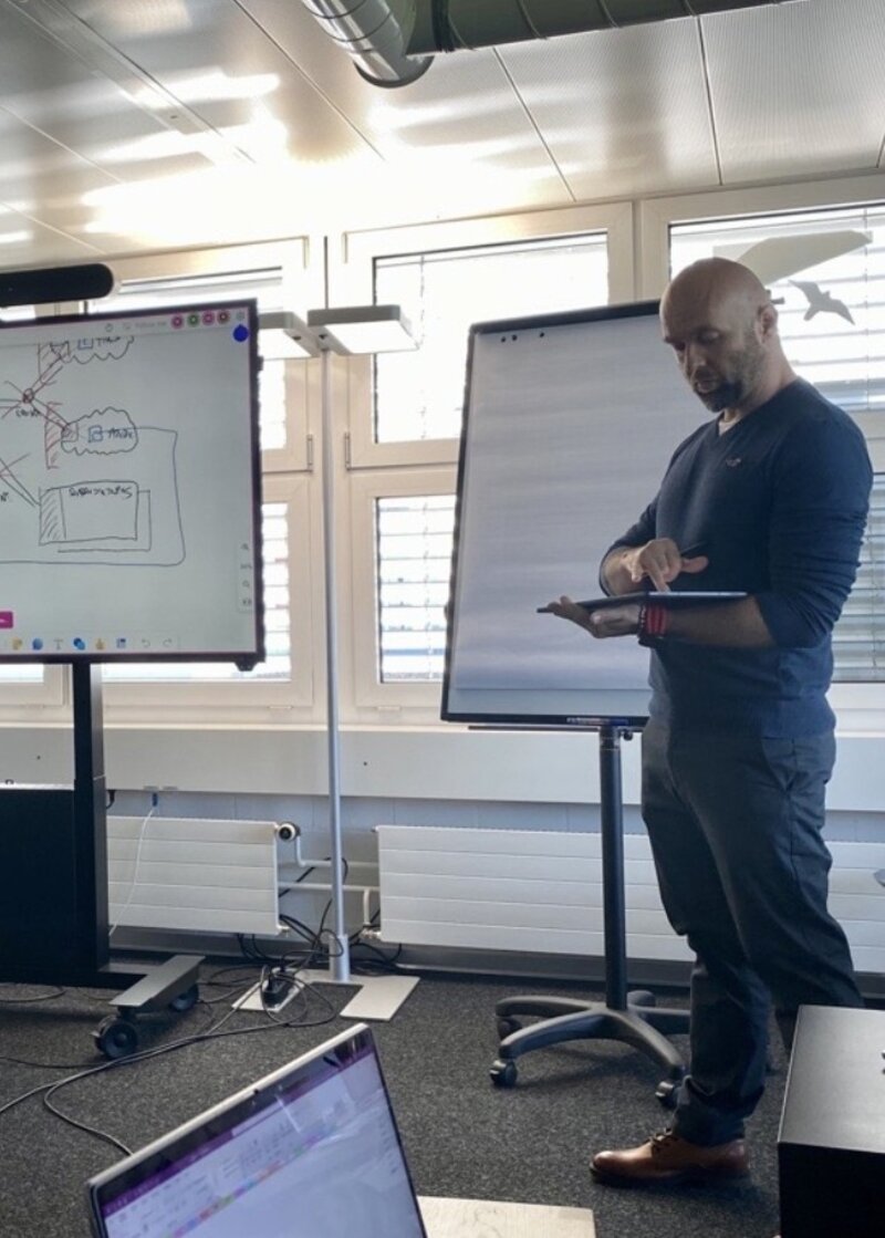 A presenter using a tablet beside a network diagram and flip chart
